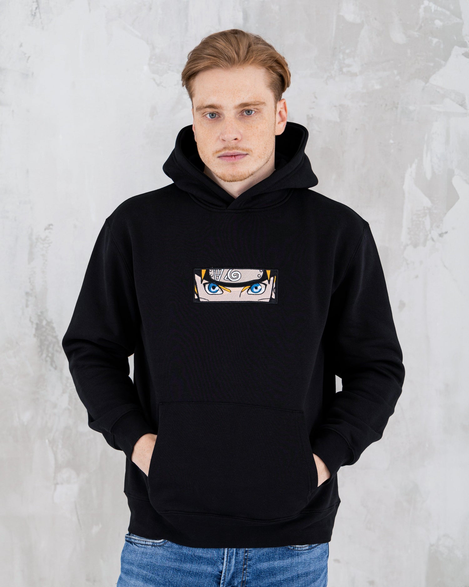 Black hoodie with Naruto anime character eyes design, worn by man against textured wall